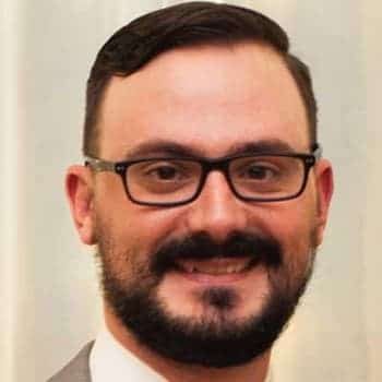 a man with glasses and a beard wearing a suit.