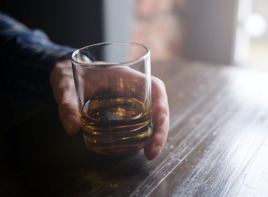 a person holding a glass of whiskey on a table.