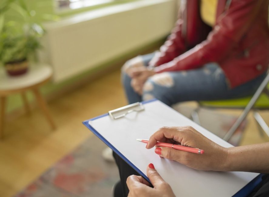 a woman sitting on a couch writing on a piece of paper.