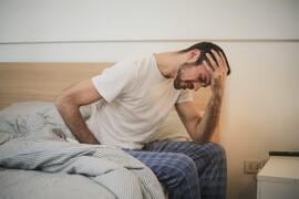 a man sitting on a bed with his head in his hands.