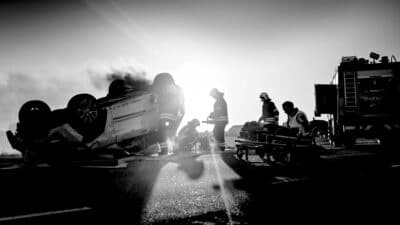 a black and white photo of a firefighter standing next to a burning car.